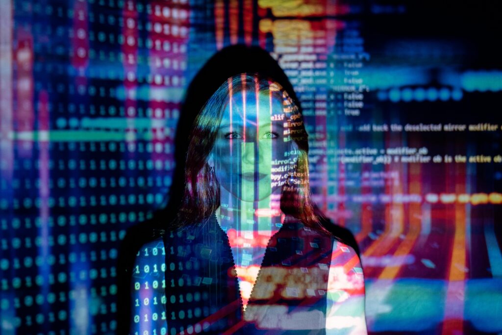 person with long hair, dressed in a dark outfit, standing in front of a vibrant, digital background